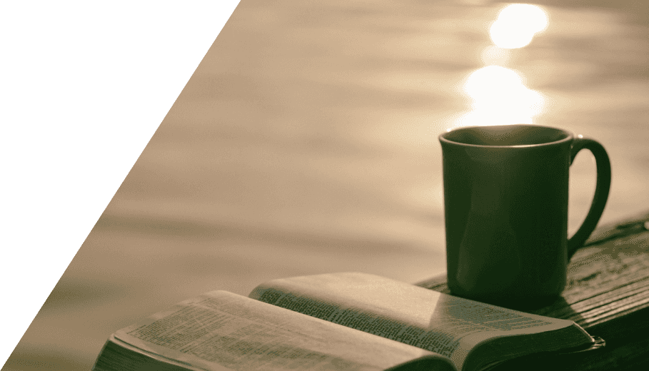 A cup of coffee and a Bible on a wooden railing by a sunny lake